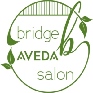 Green circular logo with the text "Bridge Aveda Salon" adorned with leaf designs, reflecting its dedication to hair care and vibrant hair color. - Bridge Aveda Salon | Chattanooga, TN